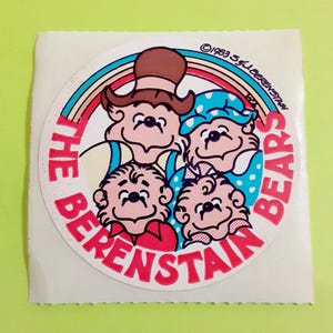 May include: A vintage sticker featuring the Berenstain Bears family. The circular design includes the text "THE BERENSTAIN BEARS" in red, surrounding a cartoon illustration of the bear family. A rainbow arches over the bears. Copyright 1983 S.J. Berenstain.