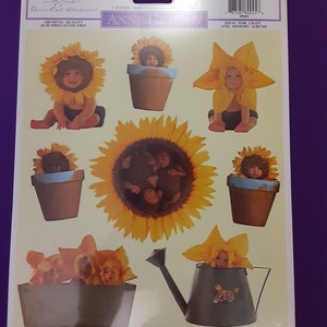 Puede incluir: Una hoja de pegatinas con ocho imágenes de bebés vestidos de girasoles. La hoja es blanca con un fondo amarillo y el texto "Anne Geddes" en negro.