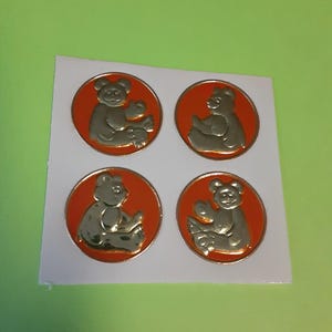May include: Four gold-colored bear stickers on a white background. Each bear is inside a red circle. The bears are in different poses, with a shiny metallic finish. The stickers are on a white, rectangular sheet.