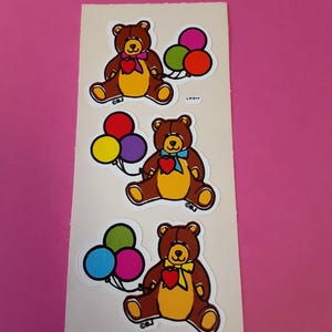 May include: Sheet of stickers featuring three cartoon teddy bears. Each bear is brown with a yellow belly, a red heart, and a bow tie. Each bear holds a bunch of colorful balloons. The stickers are on a white background.