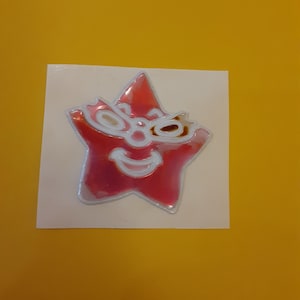 May include: A pink star-shaped sticker with a white smiling face and black eyes. The sticker has a 3D effect.