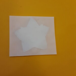 May include: A white star shape on a yellow background. The star is cut out of a piece of paper and is slightly translucent.