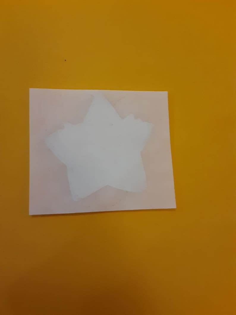May include: A white star shape on a yellow background. The star is cut out of a piece of paper and is slightly translucent.