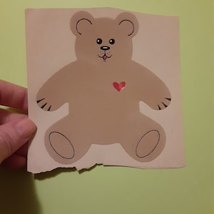 May include: A brown teddy bear with a red heart on its chest. The bear has a black nose and eyes and a pink tongue sticking out.