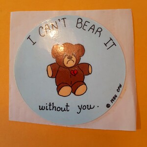May include: A round sticker with a light blue background featuring a brown teddy bear with a red heart. The text "I can't bear it without you" is written around the bear. Copyright 1984 CPN.