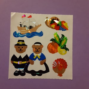 May include: A sheet of stickers featuring Thanksgiving-themed imagery. The stickers include a pilgrim bear, a pilgrim bear wearing a dress, a ship sailing on the ocean, a cornucopia, a turkey, and corn on the cob.