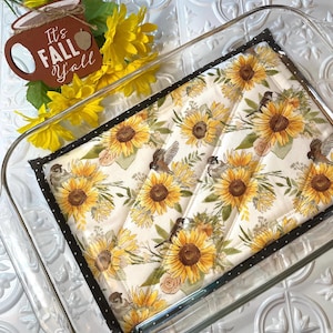 May include: A glass baking dish with a black and white quilted hot pad featuring a sunflower and bird pattern. The hot pad has the text "It's Fall Y'all" on it.