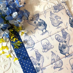 May include: Blue and white kitchen pot holder with a pattern of chickens and eggs. The pot holder has a blue and white polka dot border.