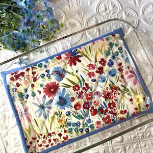 May include: A floral patterned quilted hot pad with a light blue border, placed inside a clear glass baking dish.