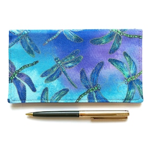 May include: A blue and purple fabric checkbook cover with a dragonfly pattern. The cover has a subtle shimmer and is accented with gold thread.