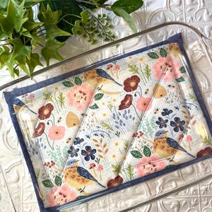 May include: A blue and white quilted hot pad with a floral and bird design. The pad is in a glass baking dish.
