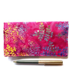 May include: A pink fabric pouch with a floral pattern in shades of yellow, blue, and gray. The pouch is closed and a pen is lying next to it.
