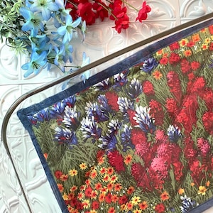 May include: A floral patterned oven mitt with a dark blue border. The mitt is made of quilted fabric and features a variety of flowers in shades of red, yellow, blue, and white.