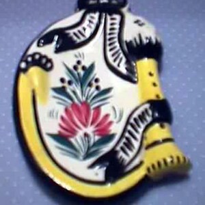 May include: A ceramic dish shaped like a woman wearing a yellow dress with black and white trim. The dish is decorated with a floral design in shades of red, green, and white.