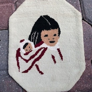 May include: A beige woven wall hanging with a red, white, and black design of a girl holding a doll. The girl has black hair and a red and white dress.