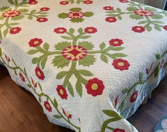 May include: A white quilt with a floral pattern in shades of red and green. The quilt is made with a traditional patchwork design and features a repeating pattern of flowers and leaves.