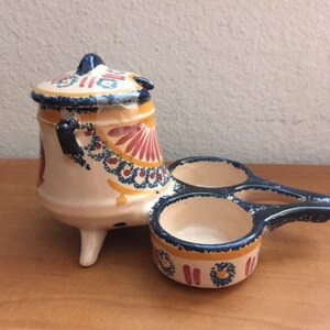 May include: A ceramic salt and pepper shaker set with a blue, red, and yellow floral design. The set features a small pot with a lid and two small bowls with handles.