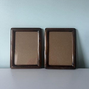 May include: Two rectangular picture frames with a dark brown wood grain finish and a smooth, polished surface. Each frame features a simple, clean-lined border surrounding a plain, light brown cardboard backing insert.