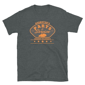 Może przedstawiać: Szary t-shirt z logo w stylu vintage dla Heemeyer's Parts & Service. Logo przedstawia traktor i tekst "Heemeyers Parts & Service" z napisem "Since 1994" i "Granby Colorado" poniżej.