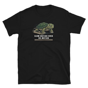 Puede incluir: Una camiseta negra de manga corta con un gráfico de una tortuga verde decidida avanzando con polvo levantándose detrás. Debajo de la tortuga, el texto dice SLOW MOTION OVER NO MOTION en letras blancas mayúsculas con una línea horizontal.