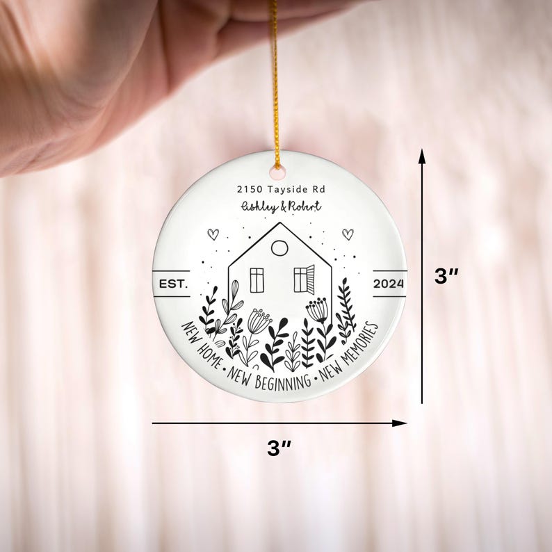 May include: A round white ceramic ornament measuring 3 inches by 3 inches, featuring a black line drawing of a house surrounded by flowers, hearts, and the text 2150 Tayside Rd, Ashley & Robert, EST. 2024, NEW HOME NEW BEGINNING NEW MEMORIES.