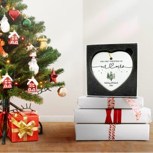 Puede incluir: Adorno navide&ntilde;o de cer&aacute;mica blanca en forma de coraz&oacute;n con el texto "Nuestra primera Navidad como Mr & Mrs" y una peque&ntilde;a ilustraci&oacute;n de dos &aacute;rboles de Navidad. El adorno est&aacute; personalizado con los nombres "Ashley & Robert" y el a&ntilde;o "2024".
