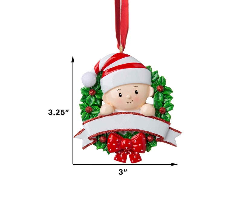 May include: A white and red baby ornament with a red bow and a green holly wreath. The ornament is 3 inches wide and 3.25 inches tall. It has a blank white banner for personalization.