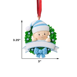 May include: A blue and white baby ornament with a green holly wreath, a blue bow, and a blank banner for personalization. The ornament is 3 inches wide and 3.25 inches tall.