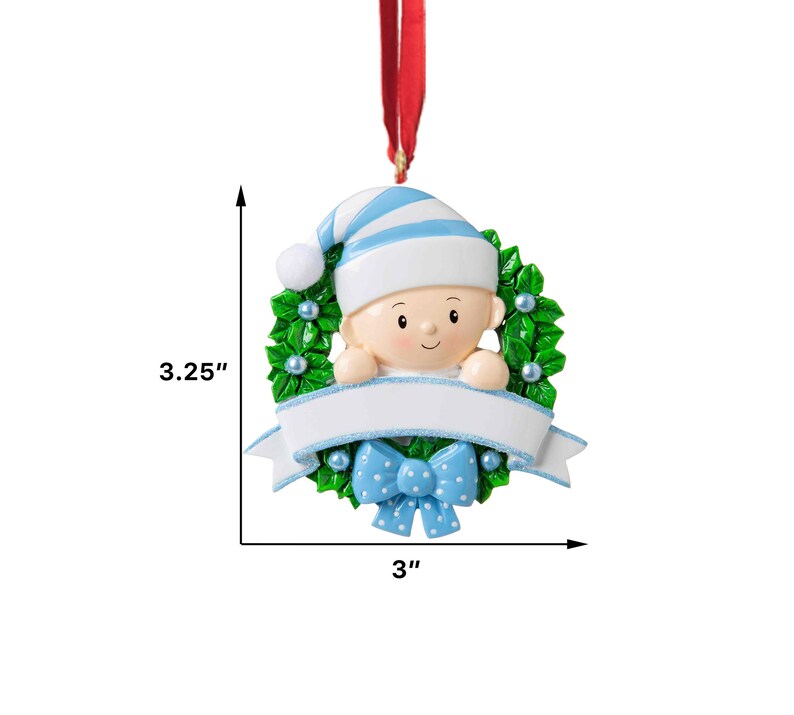 May include: A blue and white baby ornament with a green holly wreath, a blue bow, and a blank banner for personalization. The ornament is 3 inches wide and 3.25 inches tall.