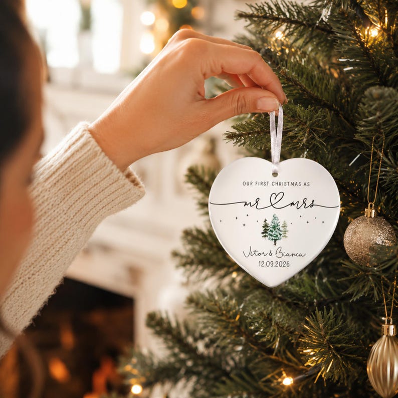 May include: A heart-shaped Christmas ornament with a white ribbon. The ornament has the text "OUR FIRST CHRISTMAS AS MR & MRS" with a small tree design and the names "Vitor & Bianca" and the date "12.09.2026".