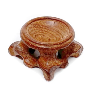 May include: A wooden orb stand with a round top and a base with four legs. The stand is made of dark brown wood with a natural grain pattern.