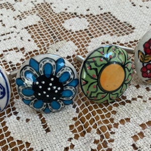 Puede incluir: Cuatro tiradores decorativos de cerámica con diseños florales. Los tiradores presentan una variedad de colores, incluyendo azul, naranja, verde y rojo, con fondos blancos. Cada tirador tiene un tornillo metálico para la fijación.