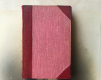 May include: A vintage hardback book with a pink linen cover and red leather spine and corners.