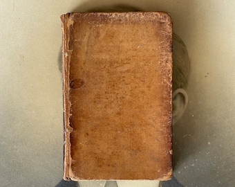 May include: A brown leather-bound book with a worn and aged appearance. The book is closed and the spine is visible.