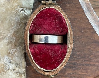 Könnte beinhalten: Ein silberner Bandring in einer roten Samtringbox. Die Box ist aus Holz und hat einen Klappdeckel.