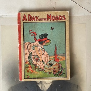 Könnte beinhalten: Ein Vintage-Kinderbuchcover mit dem Titel "A Day on the Moors". Das Cover zeigt ein Mädchen in einem rot-weiß gepunkteten Kleid, das Beeren auf einem Feld mit einer Biene und einem Schmetterling pflückt.