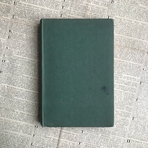 Op de afbeelding: Een donkergroen hardback boek met een effen omslag. Het boek ligt op een krant.