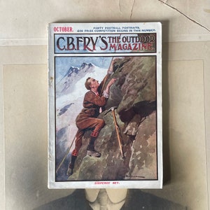 May include: A vintage magazine cover featuring a man climbing a mountain. The cover is for "C.B. Fry's The Outdoor Magazine" and the text "October. Forty Football Portraits. £50 Prize Competition Begins in This Number. Sixpence Net." is printed on the cover.