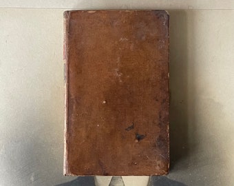 May include: A brown leather-bound book with a worn and aged appearance. The book is closed and the spine is visible.