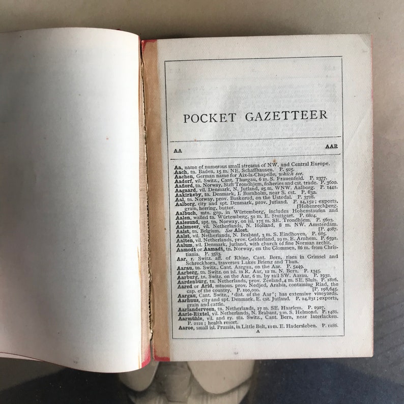 Op de afbeelding: Een pagina uit een vintage zakgazetteer met een lijst van locaties en hun beschrijvingen. De pagina is open naar de letter "A" en bevat vermeldingen voor plaatsen zoals Aach, Aken, Aadorf, Aafiord, Aagaard, Aakirkeby, Aal, Aalborg, Aalbuch, Aalen, Aalesund, Aalsmeer, Aalst, Aalten, Aalum, Aamodt of Aamadt, Aar, Aarau, Aarberg, Aarburg, Aardenburg, Aared of Arid, Aargau, Aarhus, Aarlanderveen, Aarle-Rixtel, Aarm&uuml;hle, Aaroe.