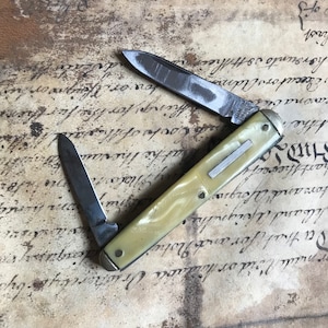 May include: A vintage pocket knife with a white handle and two blades. The knife is closed and the handle has a silver accent.