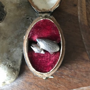 May include: A silver ring in the shape of two fish, one on top of the other, in a red velvet ring box.