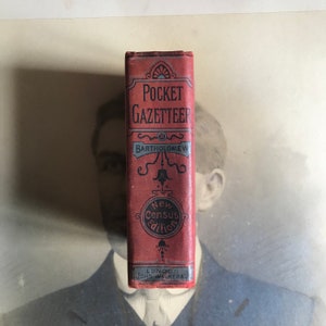 Op de afbeelding: Een rood boek getiteld "Pocket Gazetteer" door Bartholomew, met de woorden "New Census Edition" en "London John Walker & Co" gedrukt op de omslag.