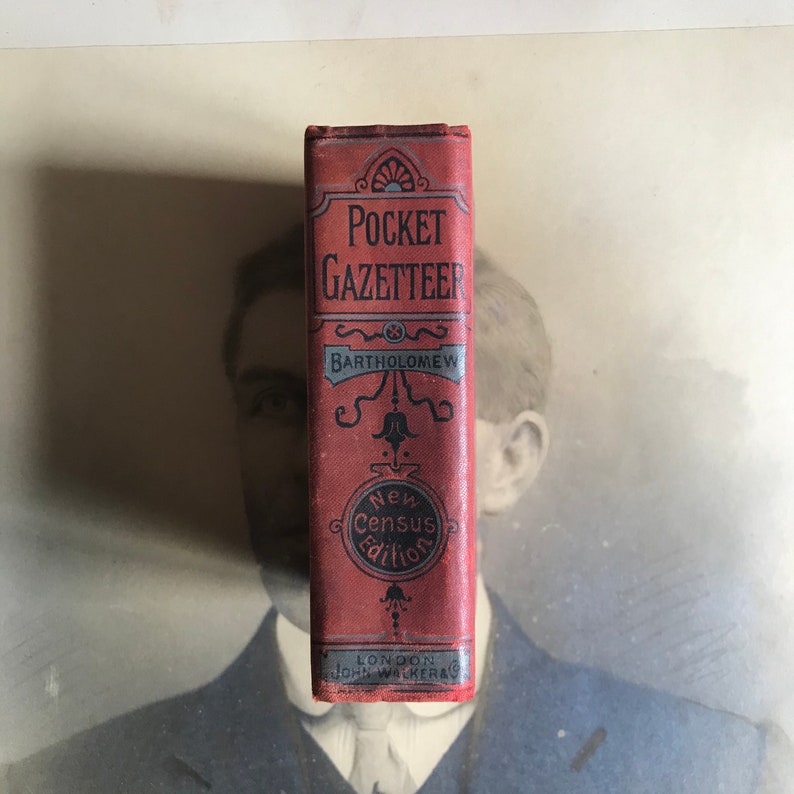 Op de afbeelding: Een rood boek getiteld "Pocket Gazetteer" door Bartholomew, met de woorden "New Census Edition" en "London John Walker & Co" gedrukt op de omslag.
