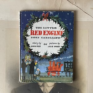 Könnte beinhalten: Ein Vintage-Kinderbuchcover mit einem roten Zug mit einem Stechpalmenkranz und dem Titel "The Little Red Engine Goes Caroling". Das Buch ist mit einem roten Zug und Sängern illustriert.
