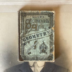 May include: An old book, "Gill's New School Geometry", with a distressed green cover and gold lettering. The book shows signs of age, with wear and tear visible. The cover includes the text "Science Subject 1." and the publisher's address.