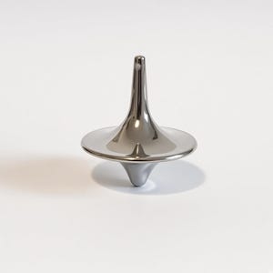May include: A polished silver-coloured metal spinning top with a smooth, reflective surface. The object features a tall, slender stem that tapers to a rounded point at the top and a wide, circular base that curves downward to a central point.