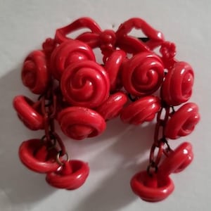 May include: A vintage red brooch with a bow and cascading spiral and circular elements. The brooch has a pin on the back for secure fastening. The design features a series of connected, stylized floral or rosette shapes, creating a unique and eye-catching accessory.
