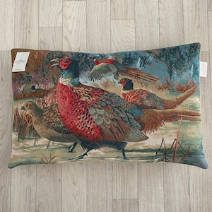 May include: Rectangular tapestry cushion featuring a detailed illustration of pheasants in a naturalistic setting. The cushion showcases a vibrant colour palette with shades of red, brown, green, and blue. The cushion measures approximately 50 cm long.
