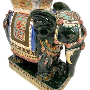 May include: A green ceramic elephant garden stool with intricate details and colorful floral patterns. The elephant has a square top and a base with a decorative border.